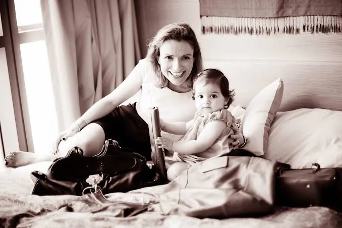 Sepia photograph of Claire with her first daughter on a bed among travel bags