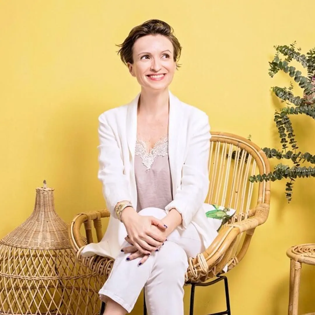 Claire Sancelot seated in a rattan chair against a yellow wall